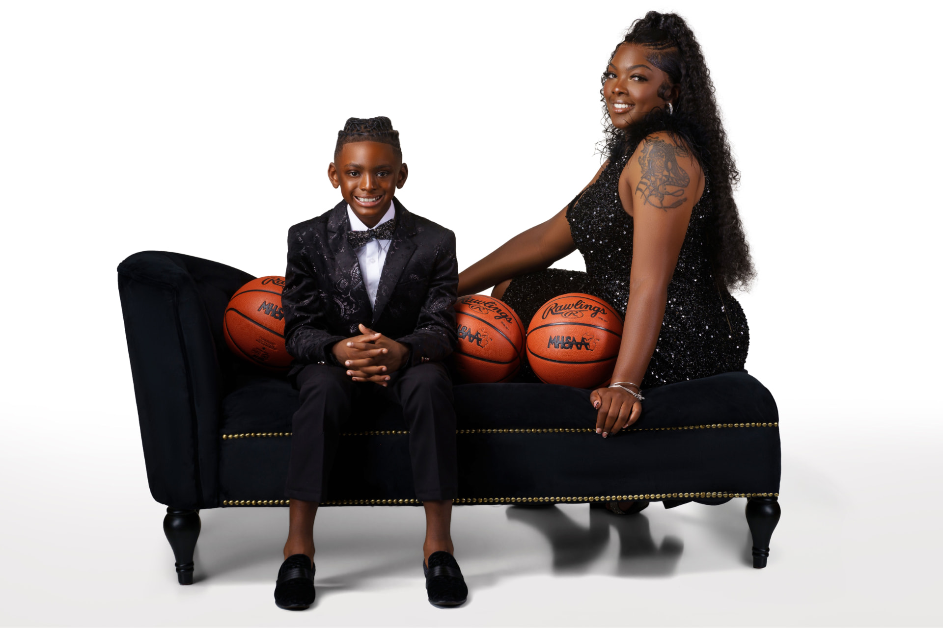 The founders of Side By Side Mobile Hoops seated together on a black bench with basketballs lined up between them.