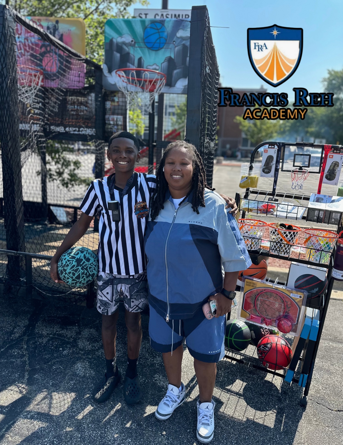 Side By Side crew member with a Francis Reh Academy staff member next to the hoops trailer and the prize rack.